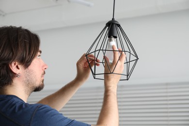 Photo of Man changing light bulb in stylish lamp indoors