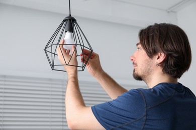 Photo of Man changing light bulb in stylish lamp indoors