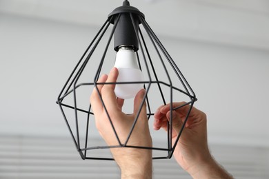 Photo of Man changing light bulb in stylish lamp indoors, closeup