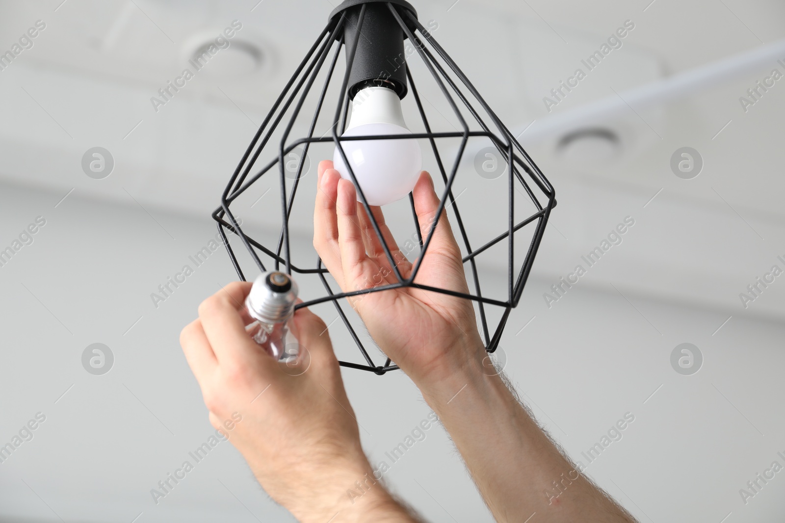 Photo of Man changing incandescent light bulb for fluorescent one in lamp at home, closeup