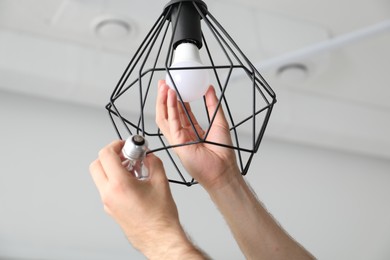 Photo of Man changing incandescent light bulb for fluorescent one in lamp at home, closeup