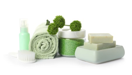 Photo of Rolled fresh terry towel, cosmetic products, brush and green flowers isolated on white