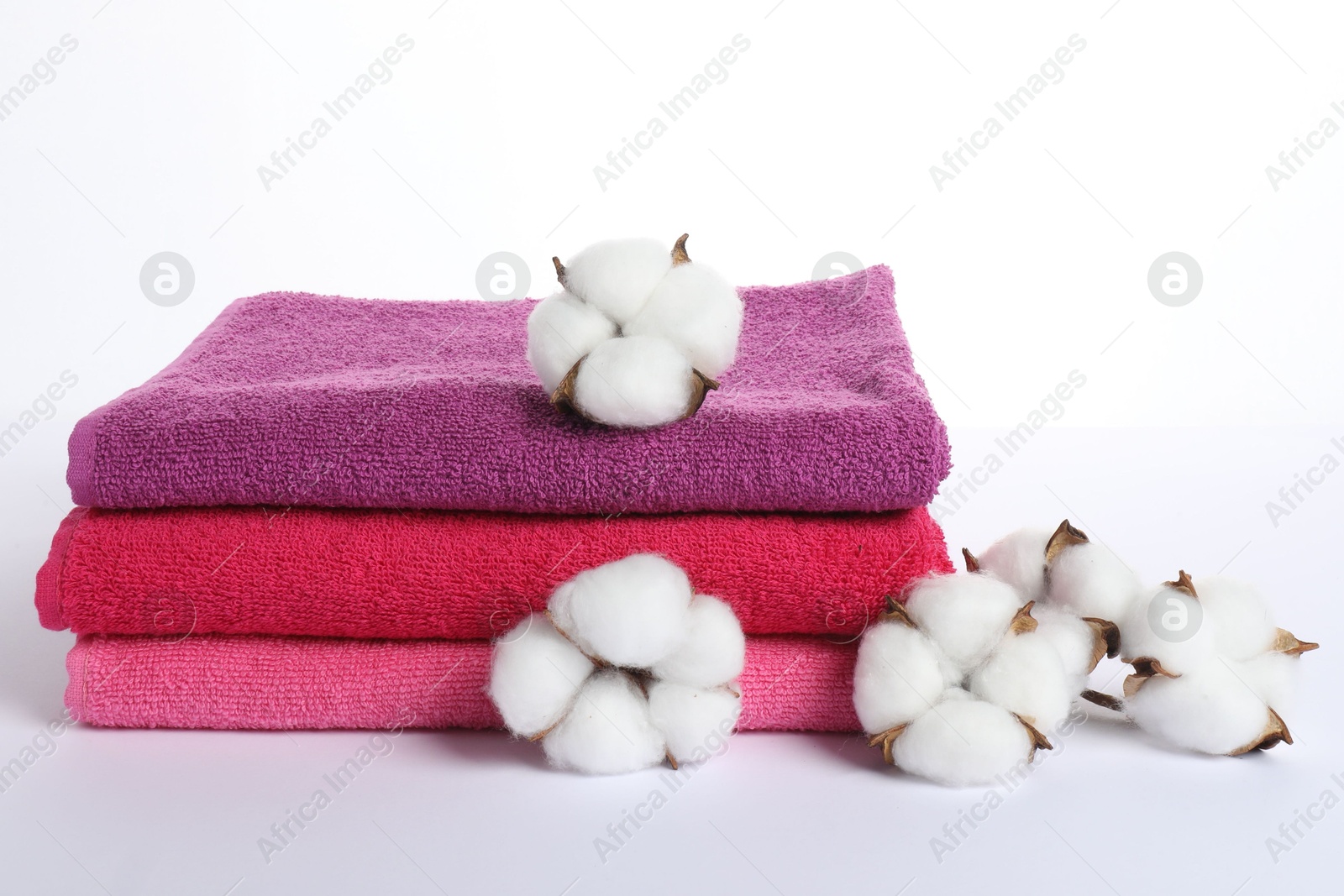 Photo of Stack of fresh terry towels and cotton flowers isolated on white
