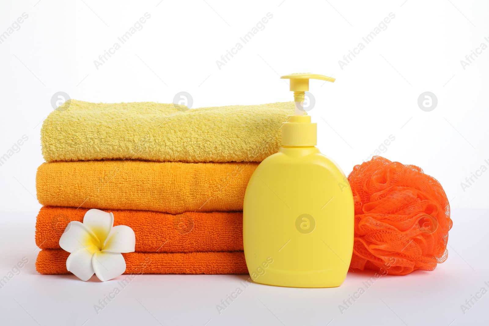 Photo of Stack of fresh terry towels, cosmetic product, sponge and plumeria flower isolated on white