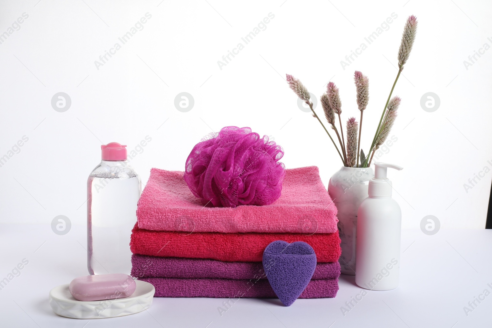 Photo of Stack of fresh terry towels, cosmetic products, sponges and floral decor isolated on white
