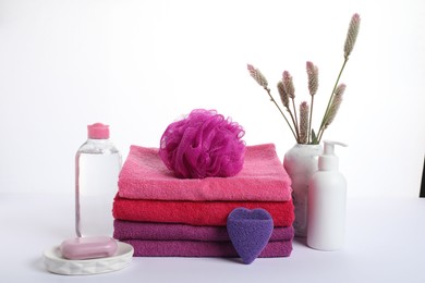 Photo of Stack of fresh terry towels, cosmetic products, sponges and floral decor isolated on white