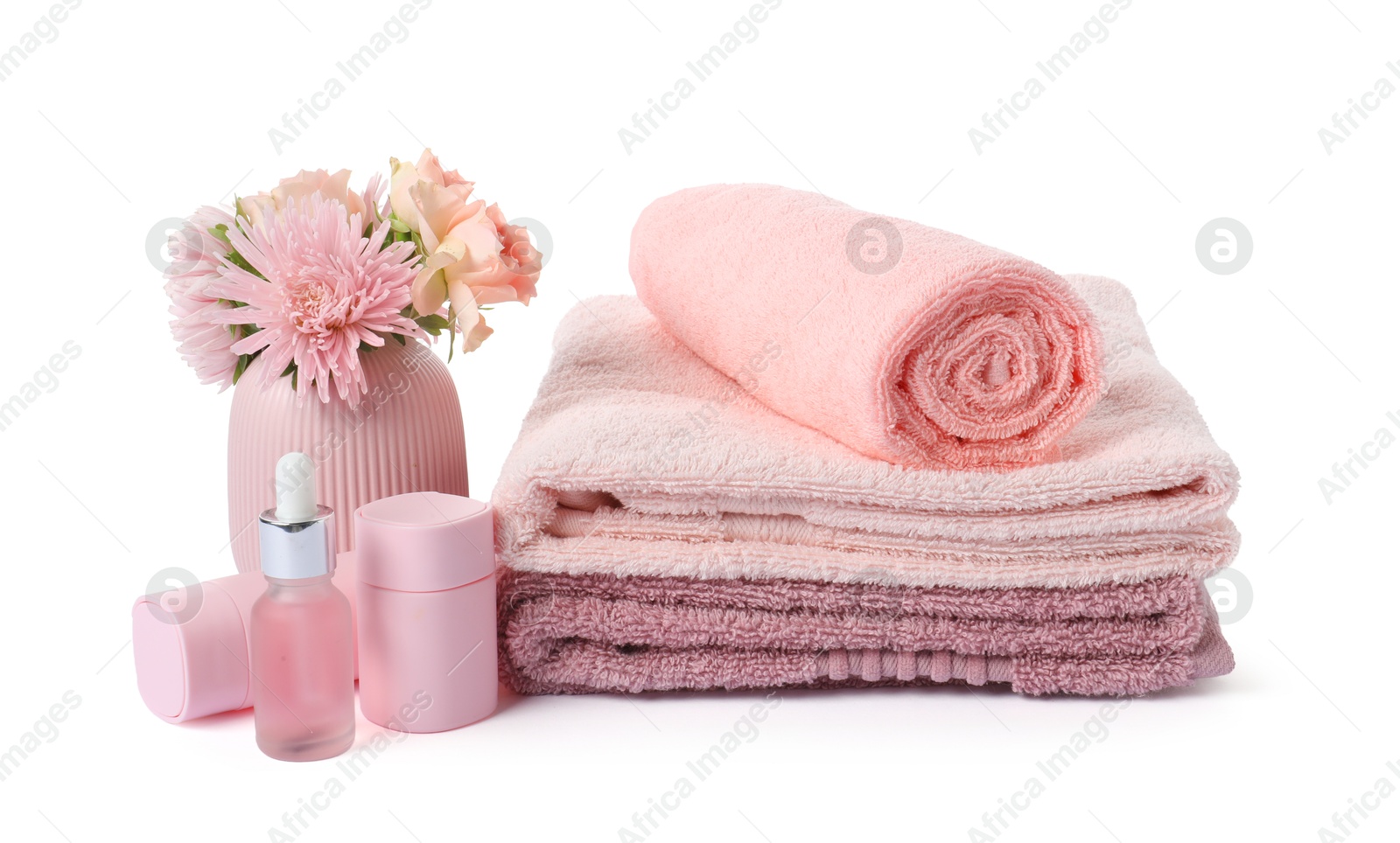 Photo of Stack of fresh terry towels, cosmetic products and flowers isolated on white