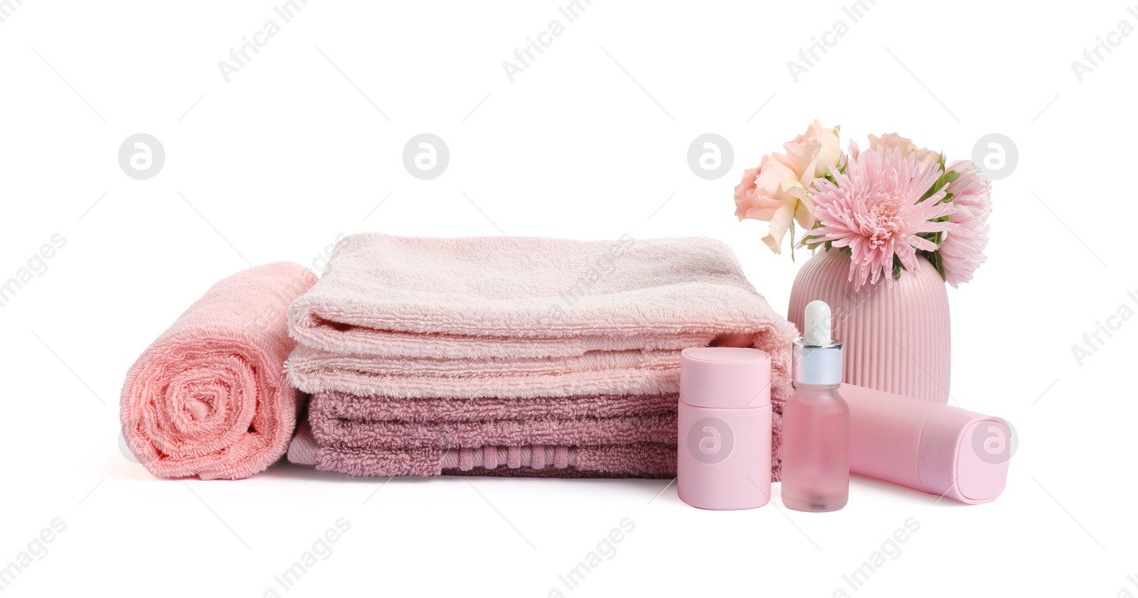 Photo of Stack of fresh terry towels, cosmetic products and flowers isolated on white