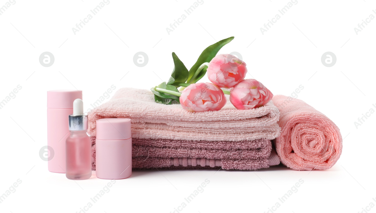 Photo of Stack of fresh terry towels, cosmetic products and flowers isolated on white