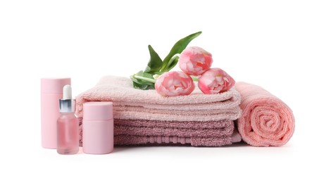 Photo of Stack of fresh terry towels, cosmetic products and flowers isolated on white