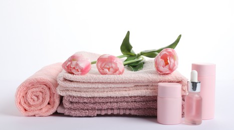 Photo of Stack of fresh terry towels, cosmetic products and flowers isolated on white
