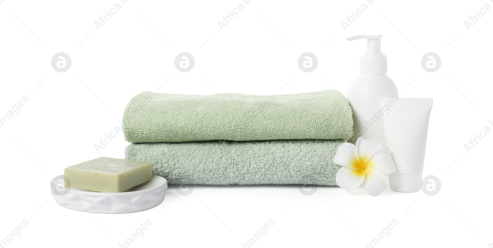 Photo of Stack of fresh terry towels, cosmetic products and plumeria flower isolated on white