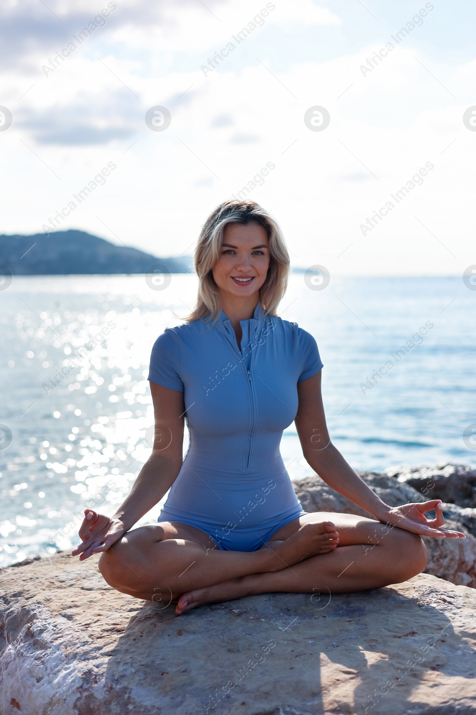 Photo of Young woman in sportswear practicing yoga on rocks at beach
