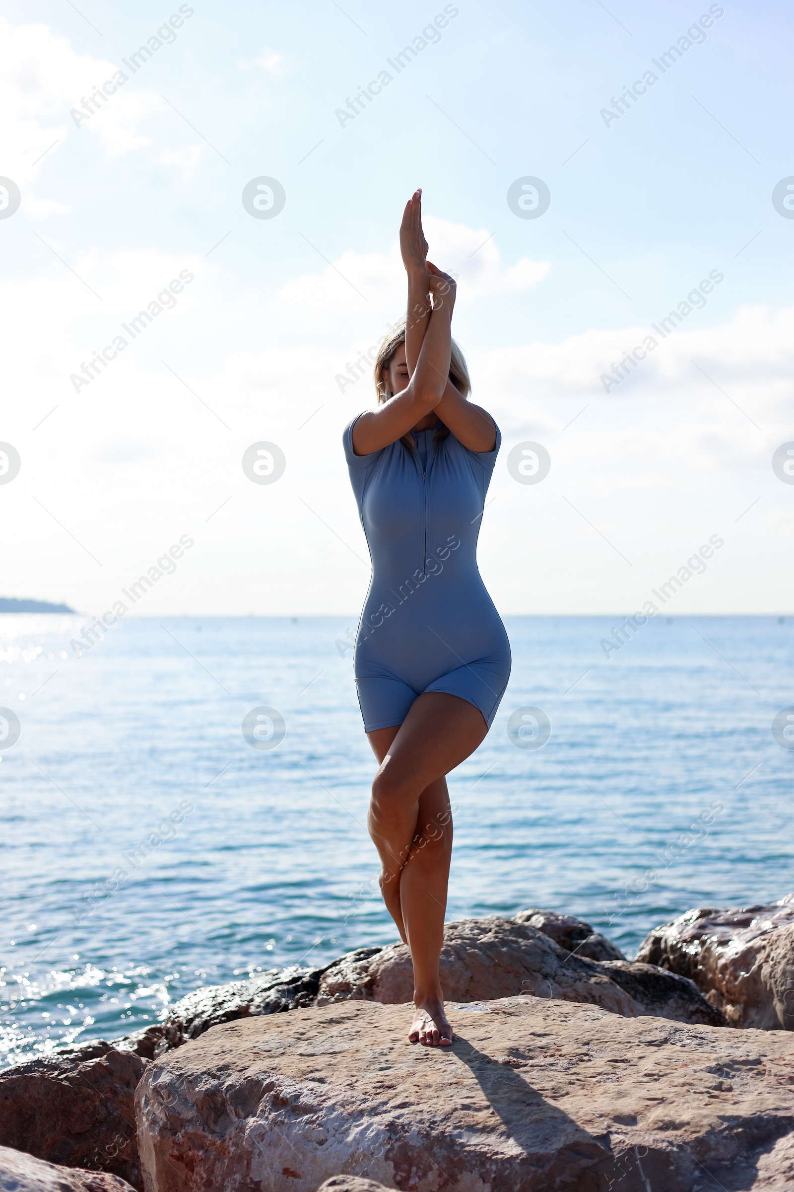 Photo of Young woman in sportswear practicing yoga on rocks at beach