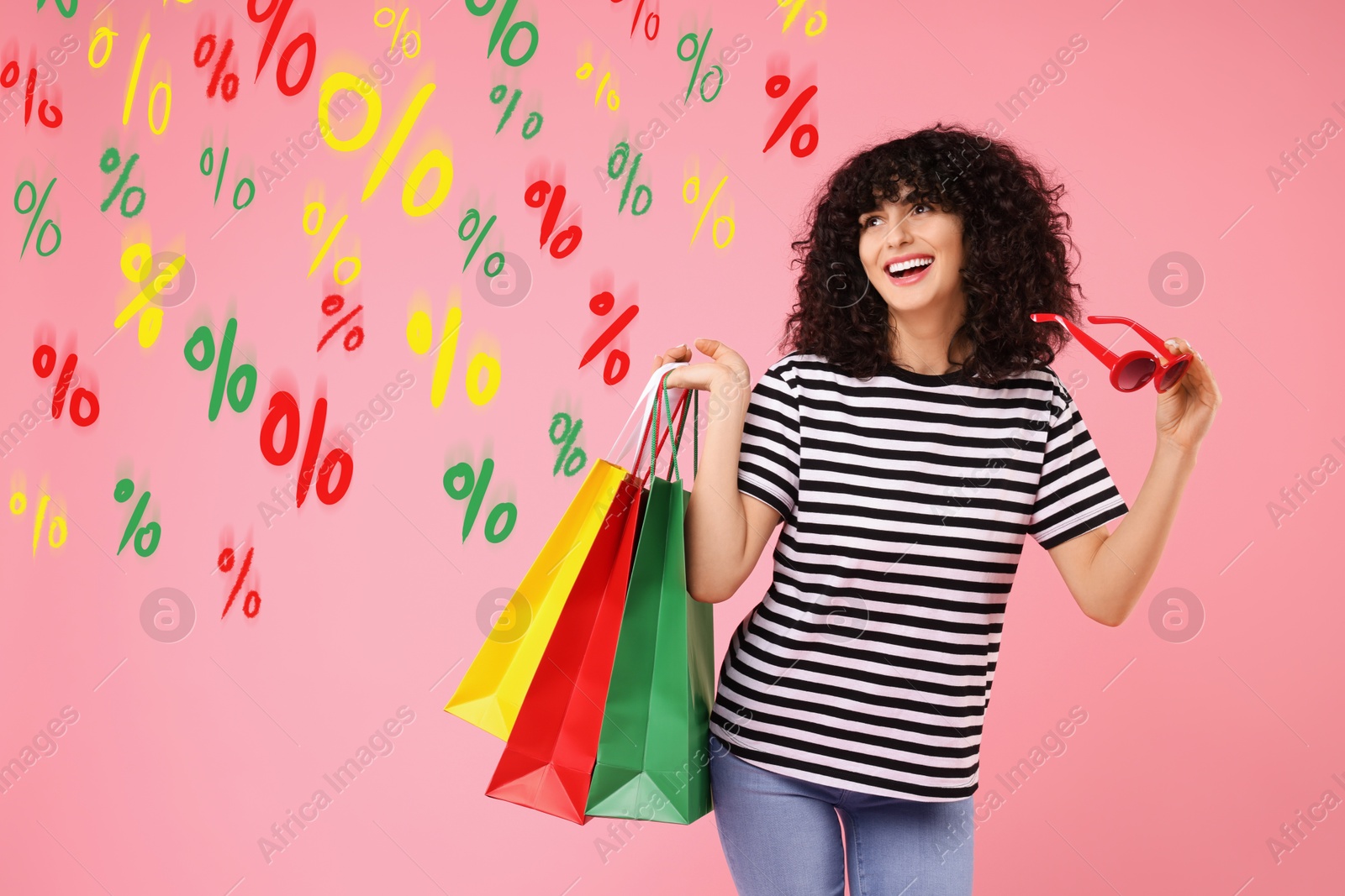 Image of Happy woman with shopping bags looking at colorful percent signs against pink background