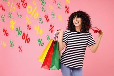 Image of Happy woman with shopping bags looking at colorful percent signs against pink background