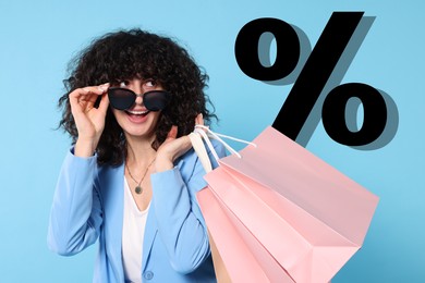 Image of Happy woman with shopping bags looking at percent sign against light blue background