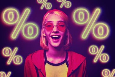 Image of Amused girl in neon light and glowing percent signs against dark purple background