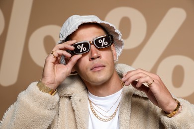 Image of Fashionable man in sunglasses with percent signs against dark beige background