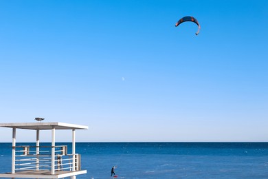 Photo of Beautiful view of wavy sea, lifeguard tower and people parasailing on sunny day