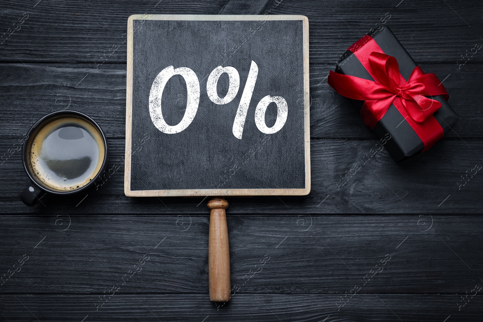 Image of Zero percent commission. Small chalkboard with 0%, gift box and coffee on black wooden background, flat lay