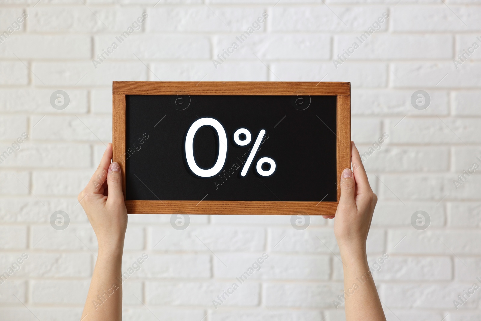 Image of Zero percent commission. Woman holding chalkboard with 0% against white brick wall, closeup