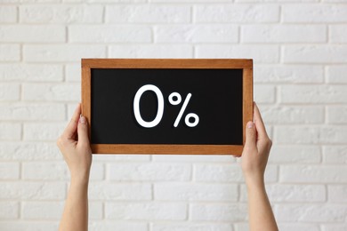 Image of Zero percent commission. Woman holding chalkboard with 0% against white brick wall, closeup
