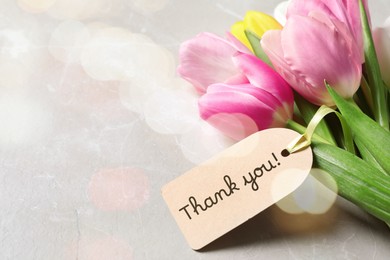 Image of Thank tag and tulip flowers on grey table. Bokeh effect