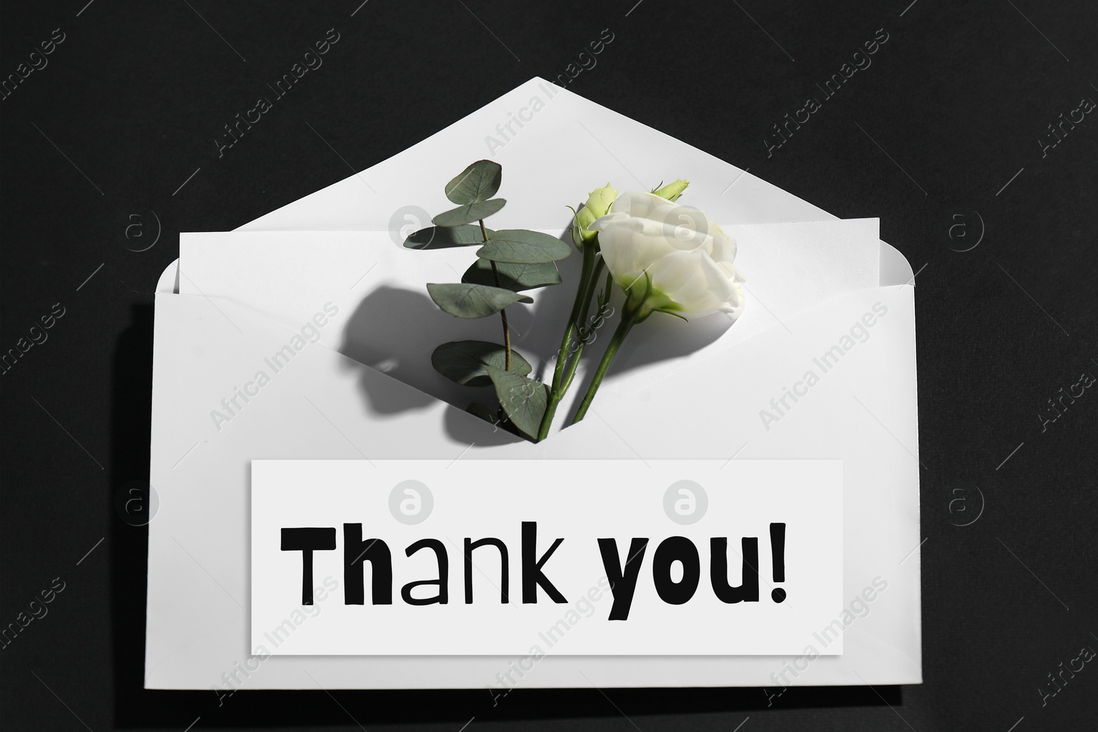 Image of Thank card and flower in envelope on black background, top view