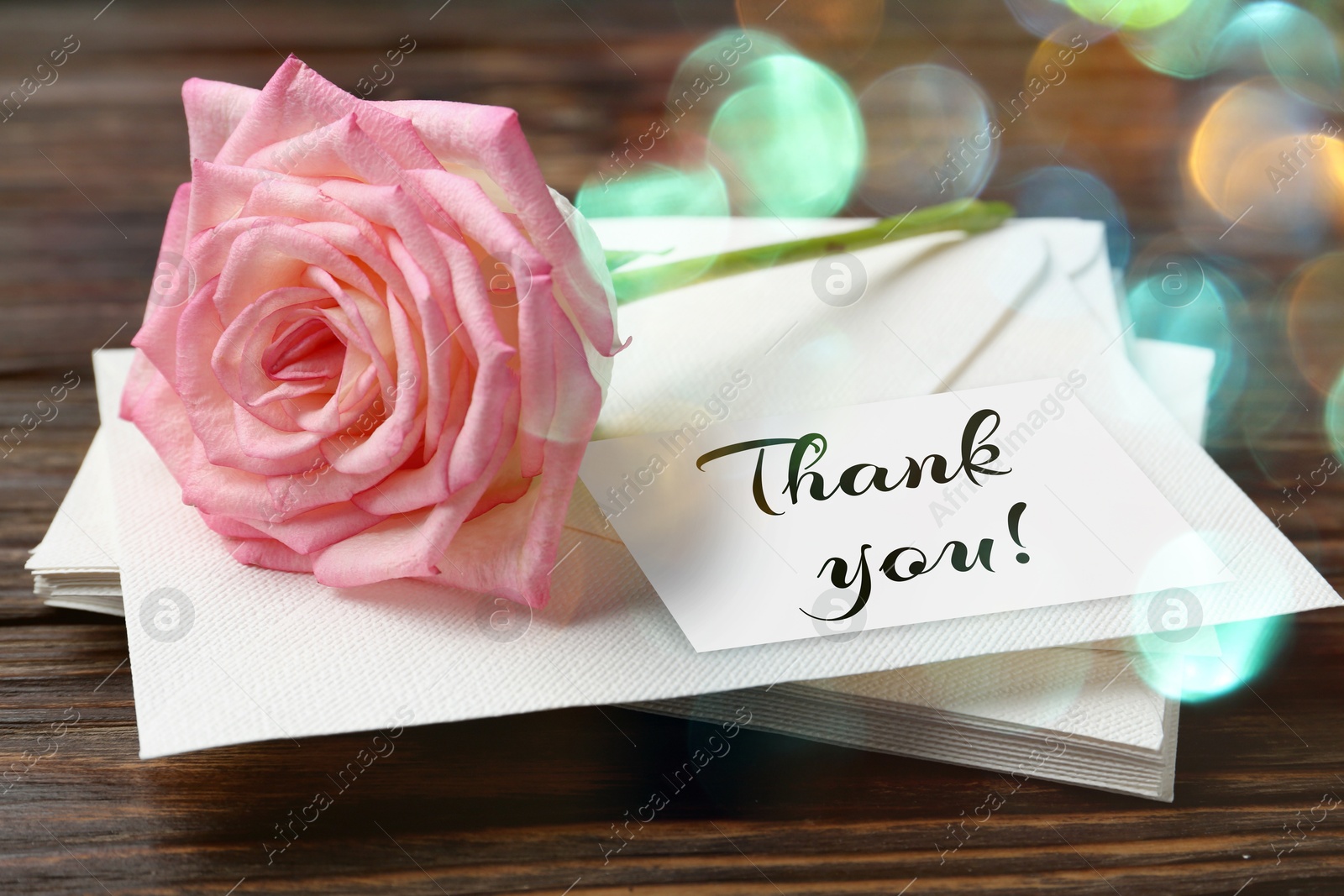 Image of Thank card, flower and stacked letters on wooden table, closeup. Bokeh effect