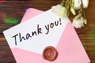Image of Thank card in envelope and flowers on wooden background, top view