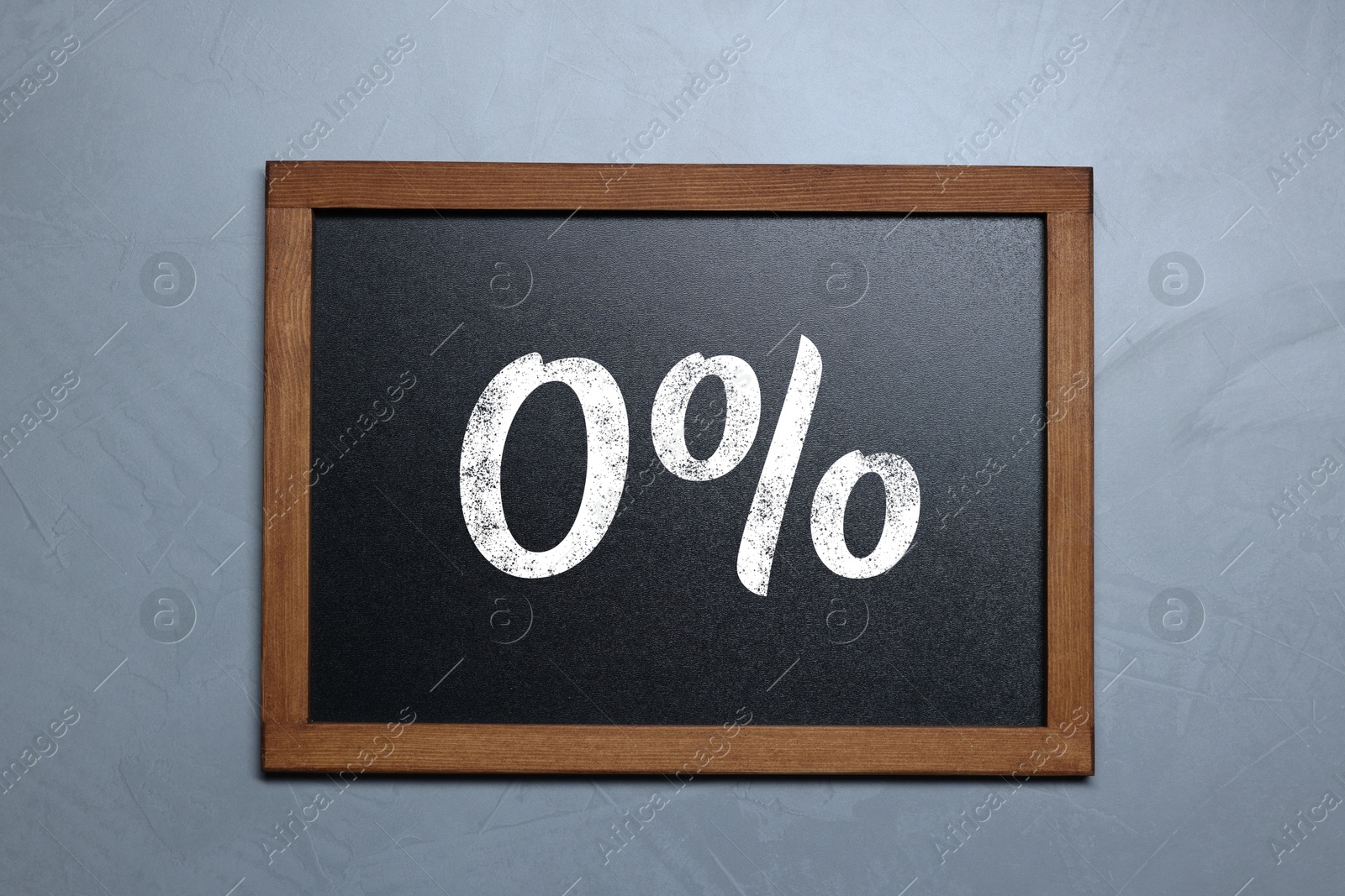 Image of Zero percent commission. Chalkboard with 0% hanging on grey wall