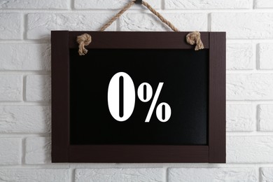 Image of Zero percent commission. Chalkboard with 0% hanging on white brick wall