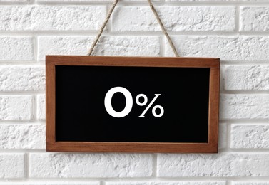 Image of Zero percent commission. Chalkboard with 0% hanging on white brick wall