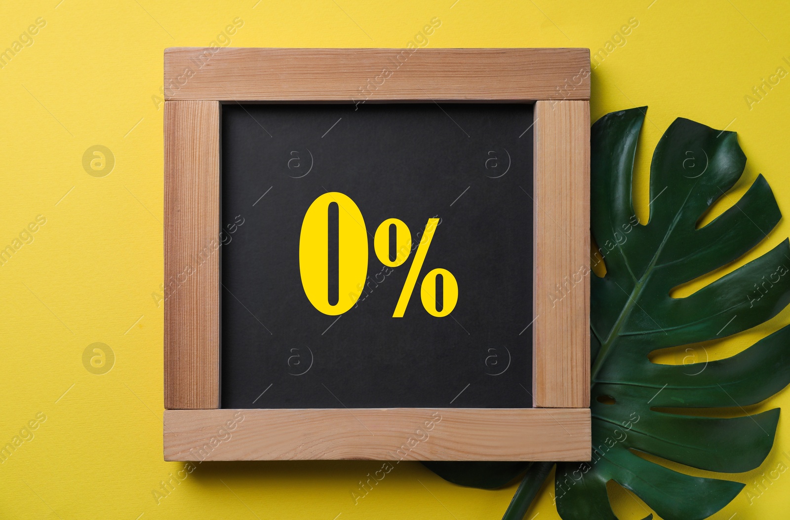 Image of Zero percent commission. Chalkboard with 0% and green leaf on yellow background, top view