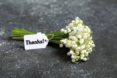 Image of Thank tag attached to bouquet of lily-of-the-valley flowers on grey textured background, closeup
