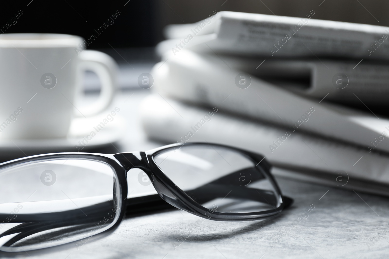 Photo of Newspapers, glasses and cup on grey table, closeup