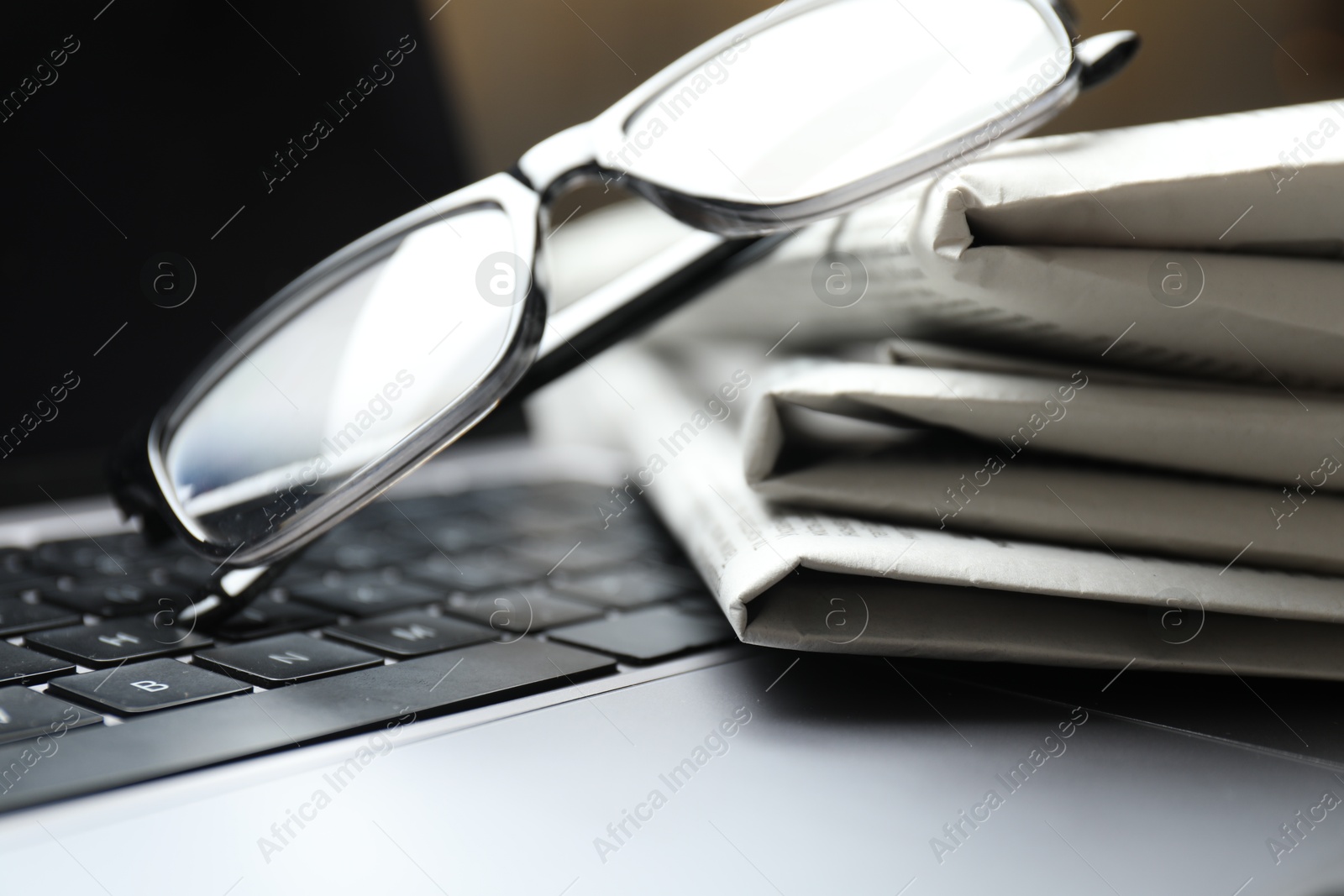 Photo of Stack of newspapers and glasses on laptop, closeup
