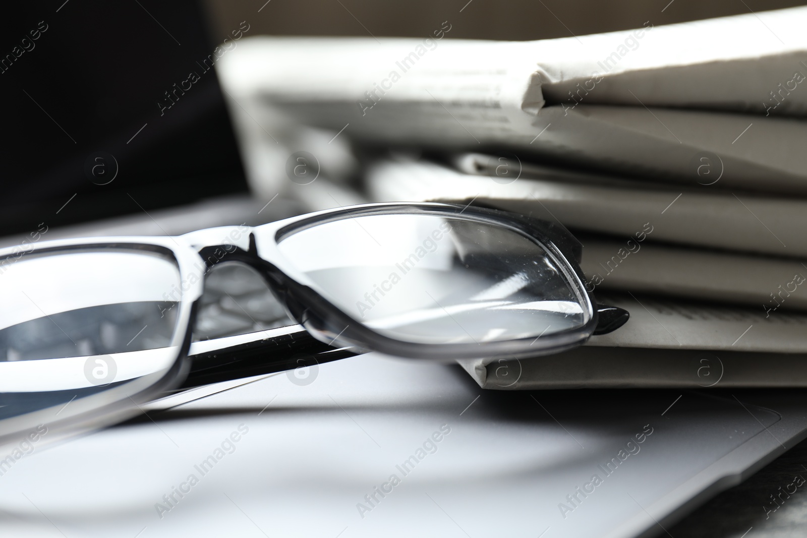 Photo of Stack of newspapers, laptop and glasses on table, closeup