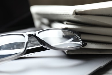 Photo of Stack of newspapers, laptop and glasses on table, closeup
