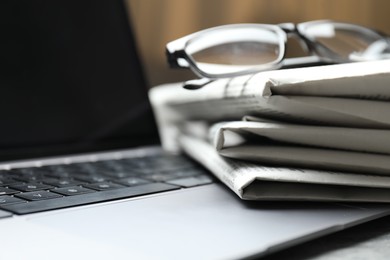 Photo of Stack of newspapers, laptop and glasses on table, closeup
