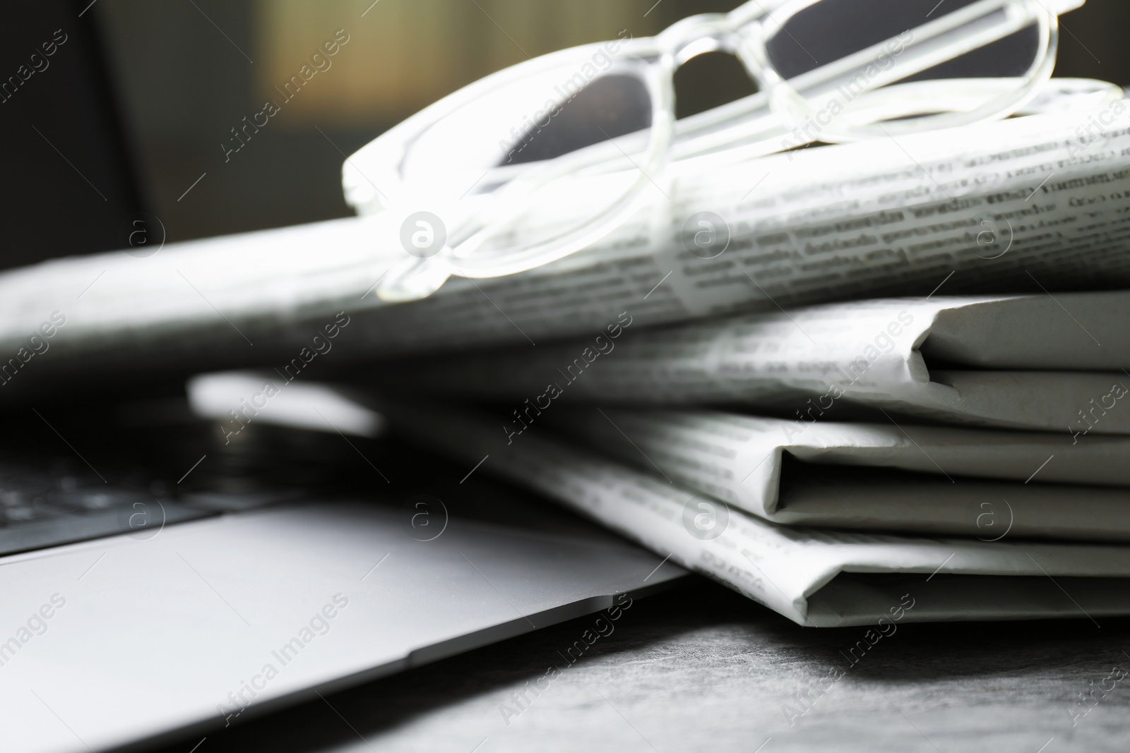 Photo of Stack of newspapers, laptop and glasses on grey table, closeup