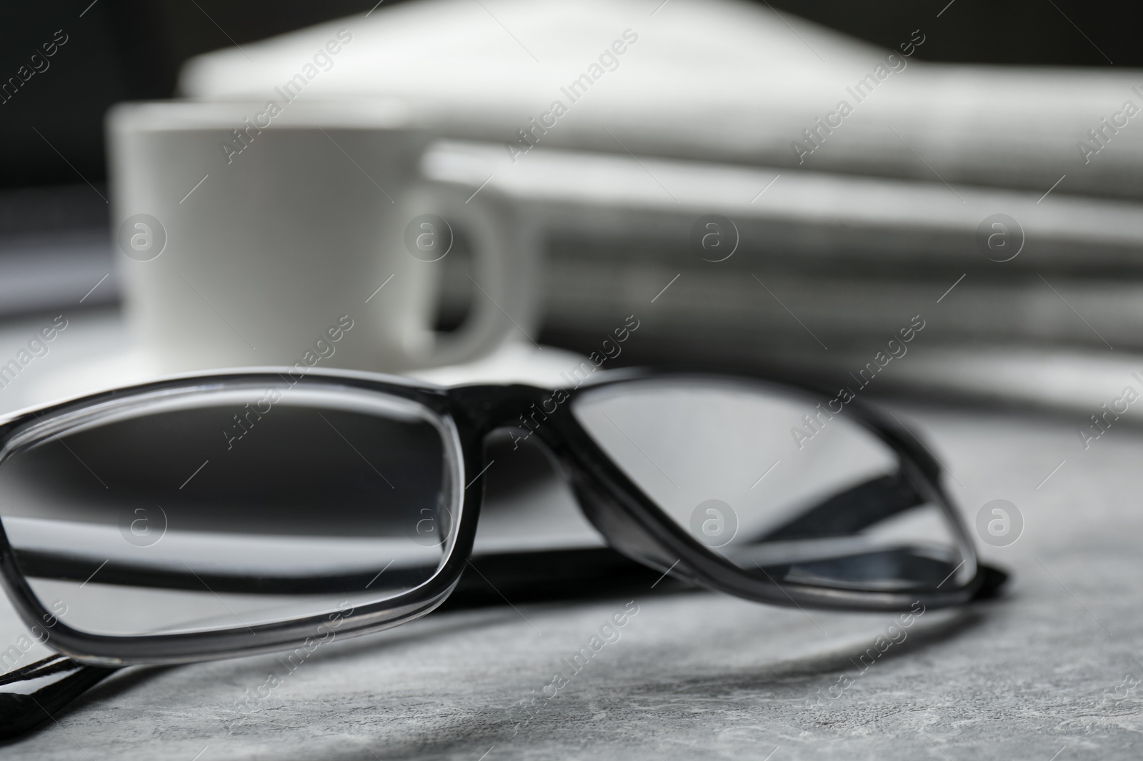 Photo of Glasses, newspapers and cup on grey table, closeup