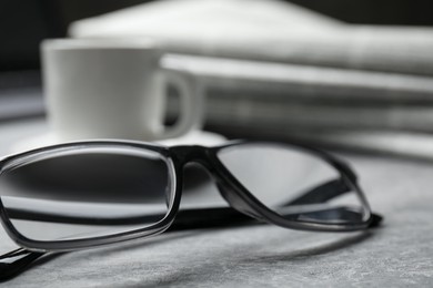 Photo of Glasses, newspapers and cup on grey table, closeup