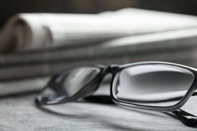 Photo of Stack of newspapers and glasses on grey table, closeup