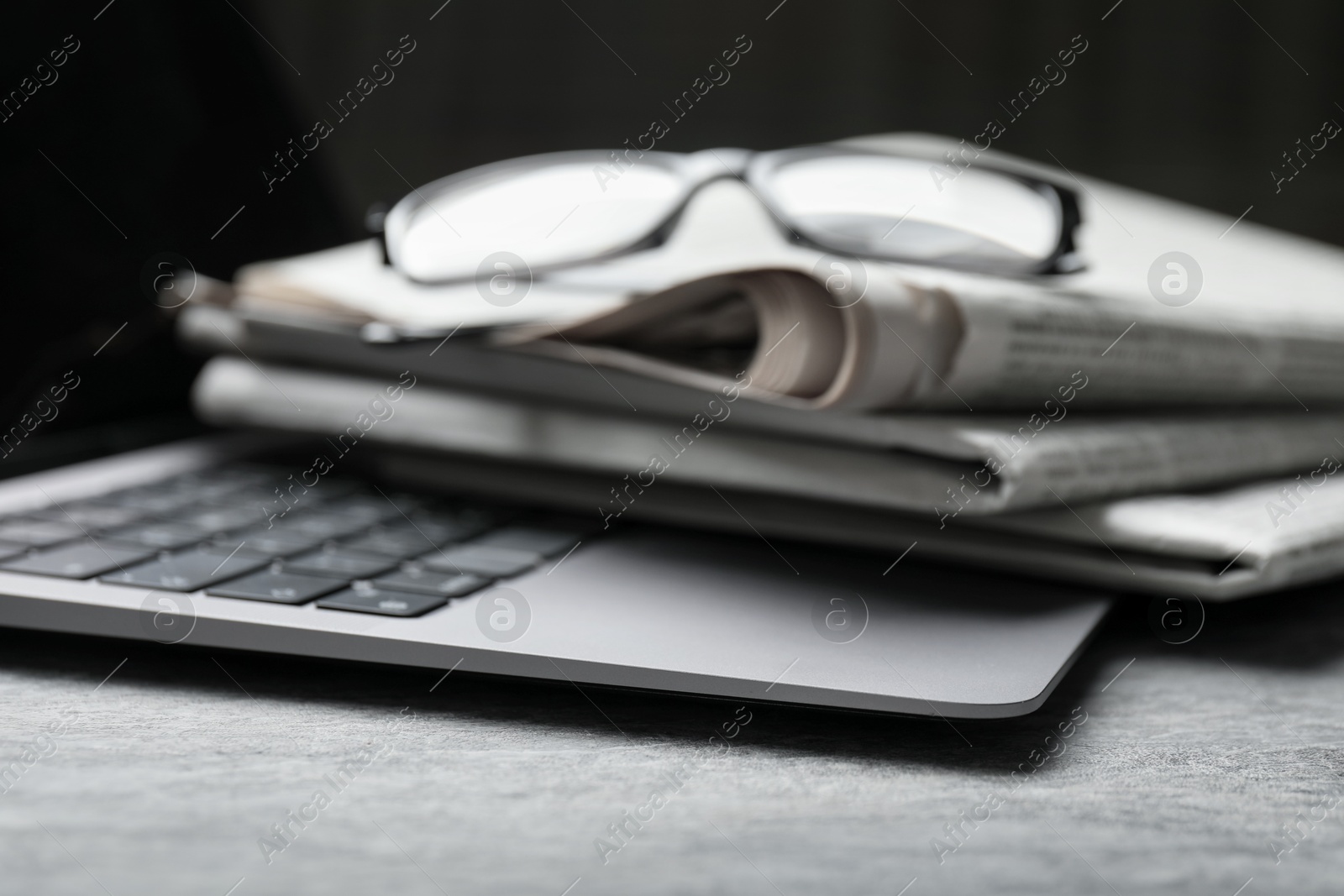 Photo of Stack of newspapers, laptop and glasses on grey table, closeup