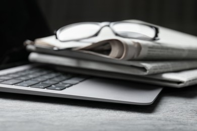 Photo of Stack of newspapers, laptop and glasses on grey table, closeup
