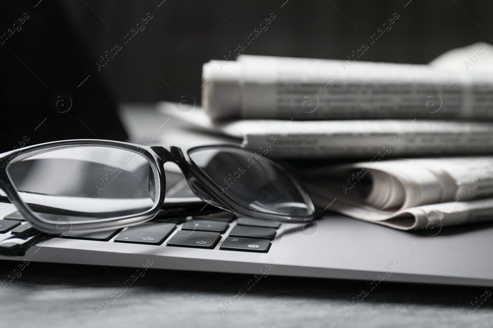 Photo of Stack of newspapers, laptop and glasses on grey table, closeup