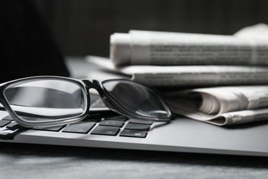 Photo of Stack of newspapers, laptop and glasses on grey table, closeup