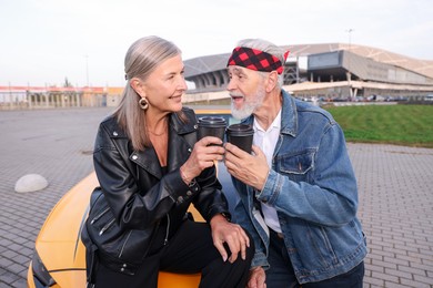 Photo of Stylish senior couple with takeaway coffee near modern cabriolet outdoors